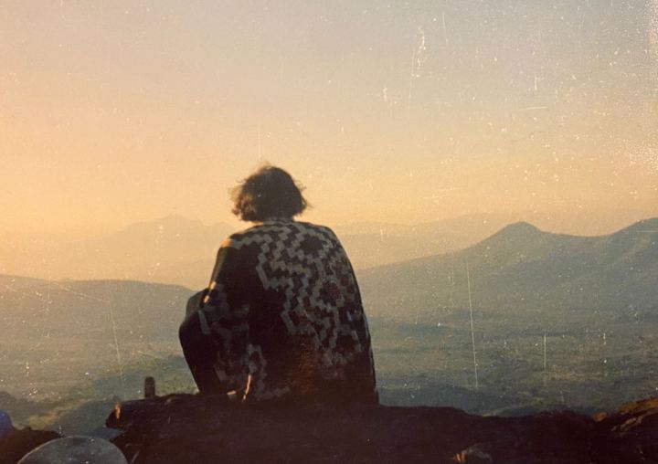 Gastón de espaldas, con poncho, mirando la puesta de sol sobre los cerros