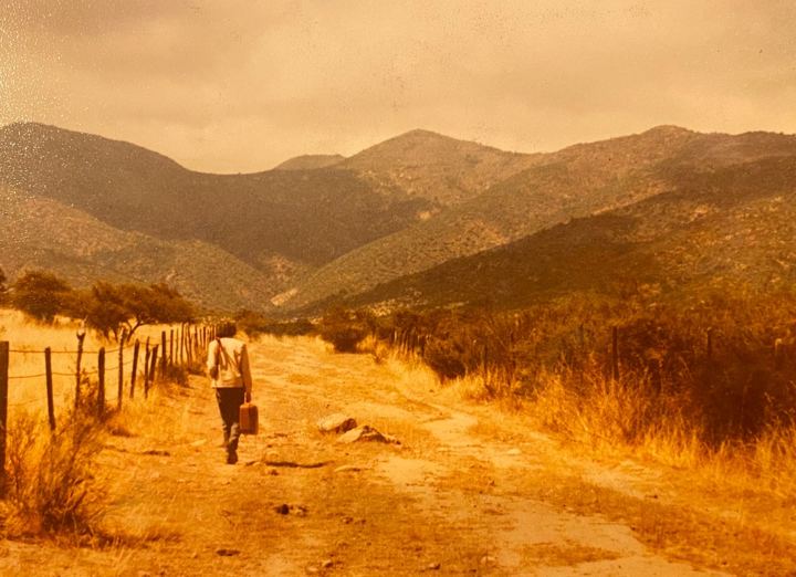 Un camino de tierra entre cerros secos, con una persona a lo lejos