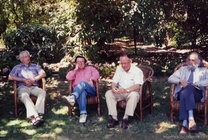 Cuatro hombres en sillones de mimbre en un jardín